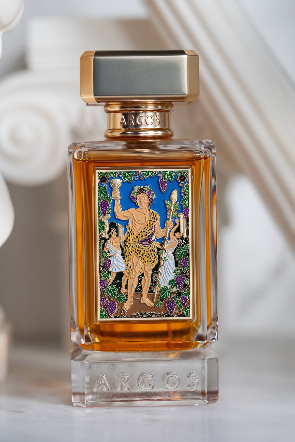 argos la dolce vita di bacchus perfume bottle with amber liquid, a detailed colorful label depicting a warrior figure, and a metallic gold cap, set against a softly blurred white background.